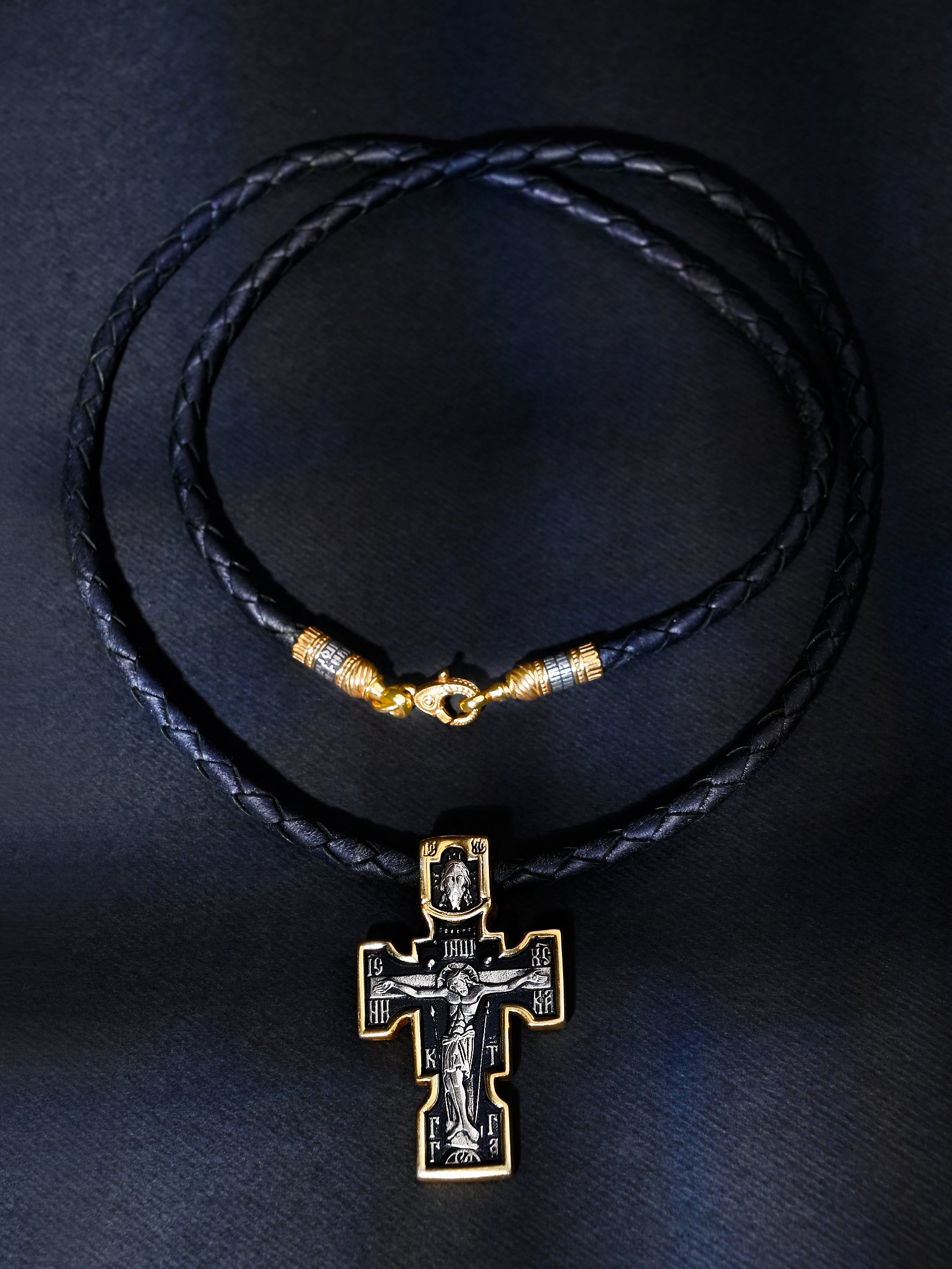 Black leather necklace with a gold and silver cross pendant on a dark background