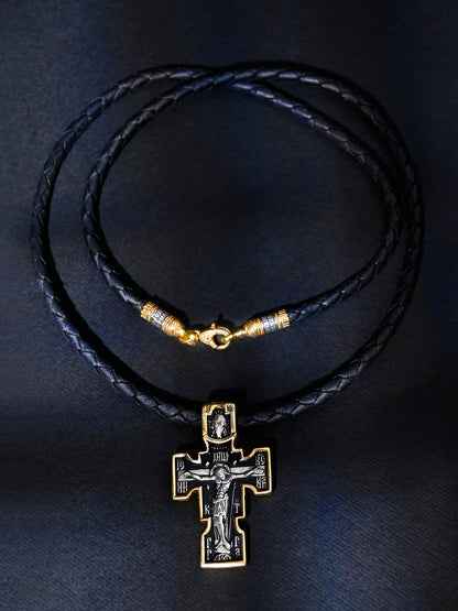 Black leather necklace with a gold and silver cross pendant on a dark background