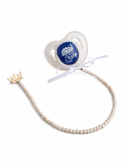 Baby pacifier with blue label and beaded chain on a white background
