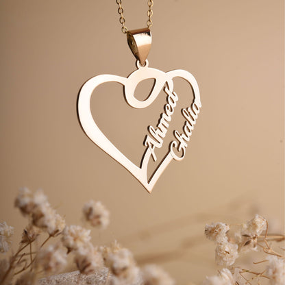 Gold heart-shaped necklace with engraved names on a beige background with dried flowers.