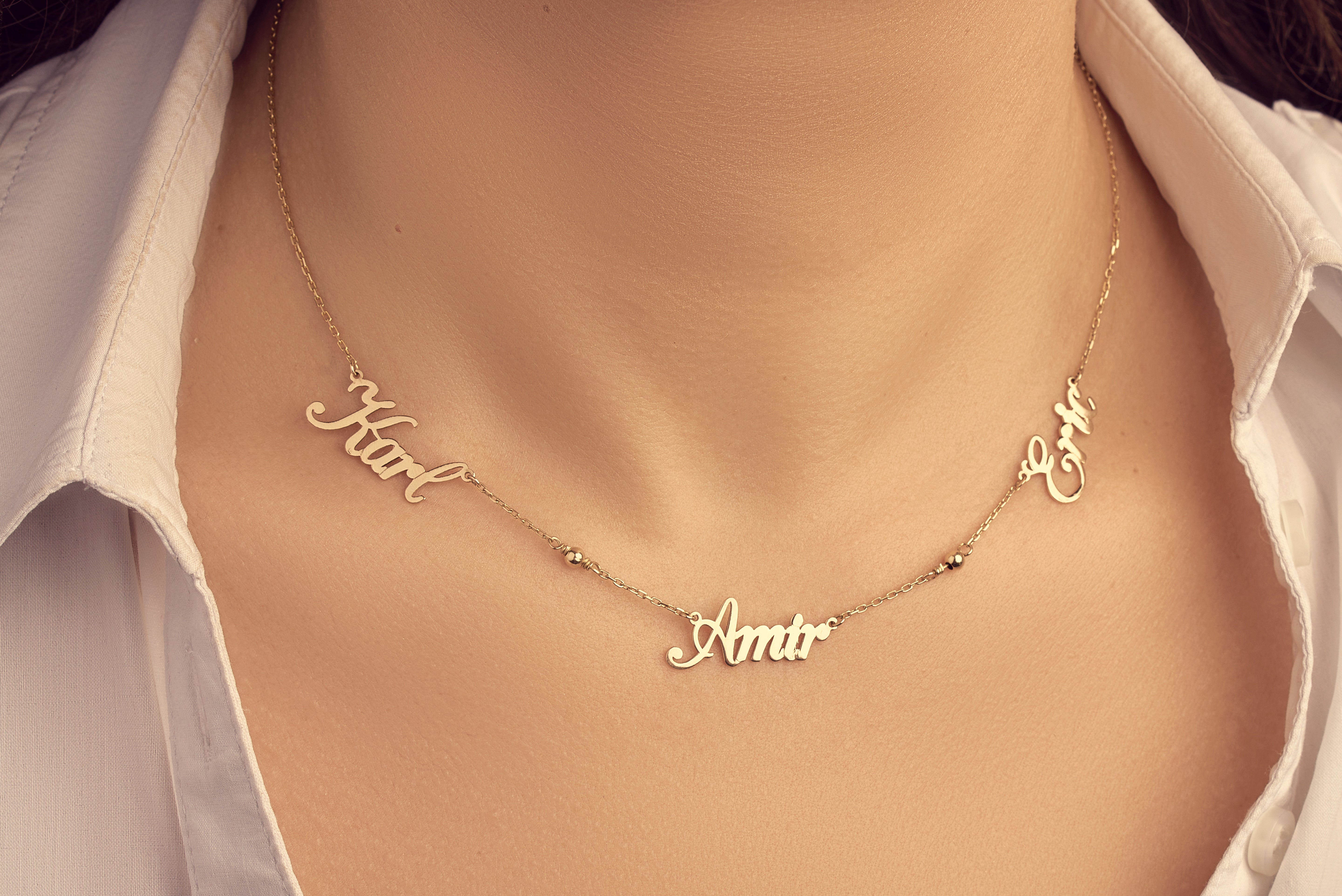 Gold necklace with name pendants on a person wearing a white shirt.