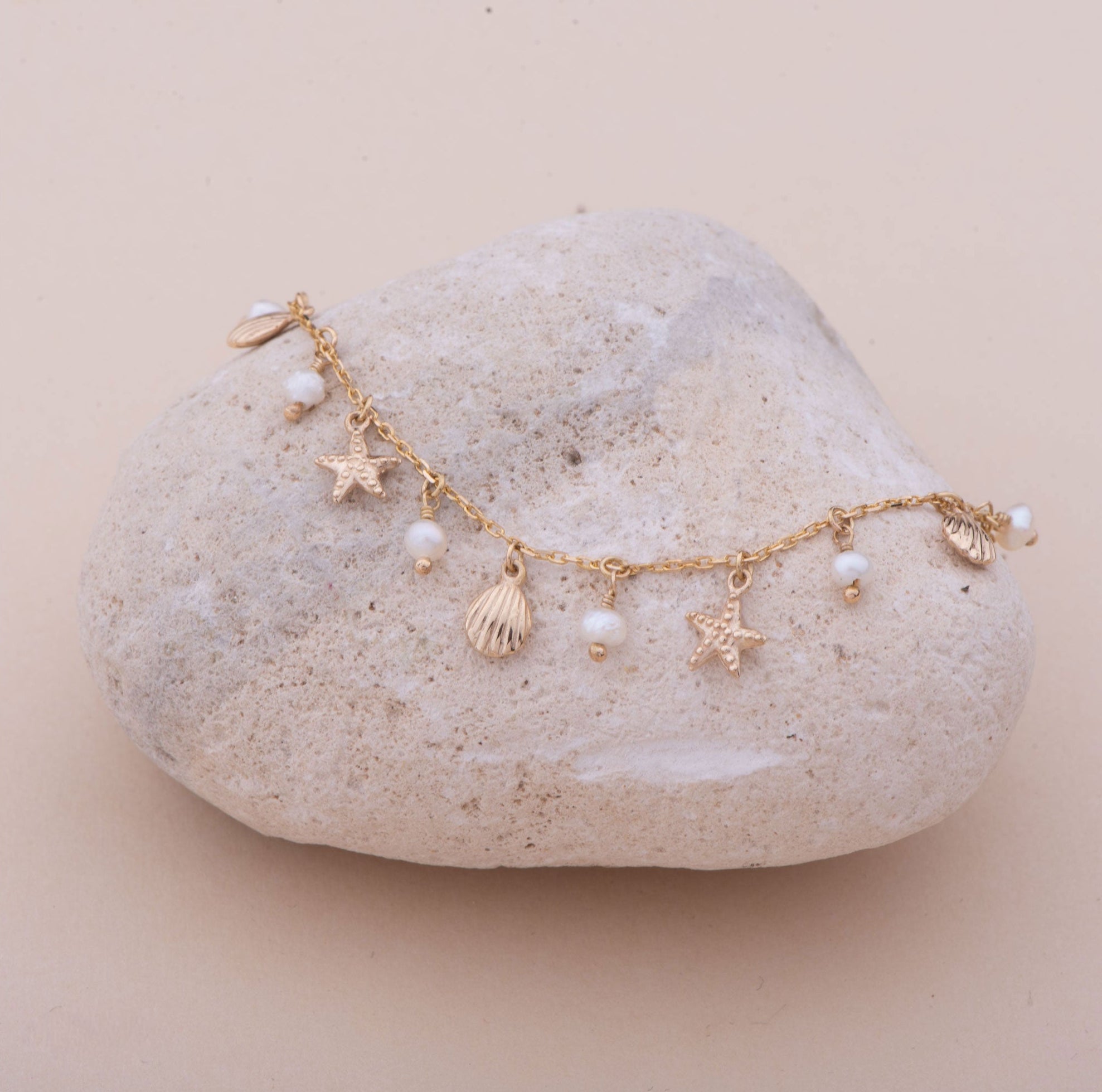 Gold bracelet with charms on a stone against a pink background
