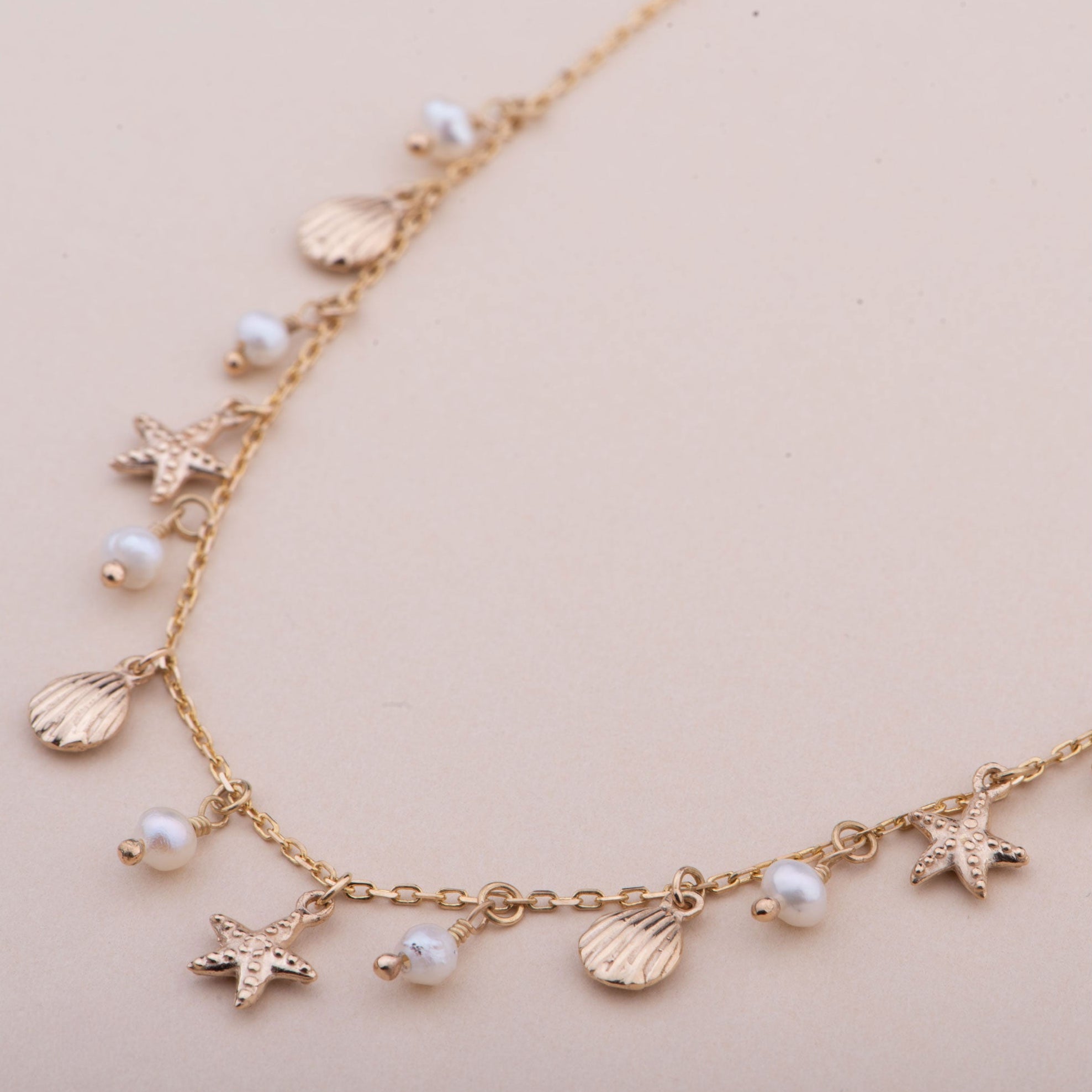 Gold necklace with starfish and shell charms on a pink card