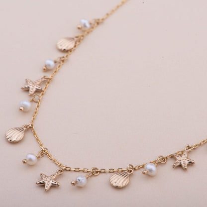 Gold necklace with starfish and shell charms on a pink card